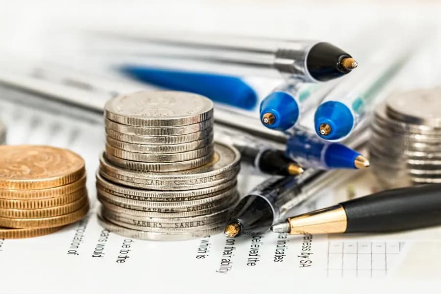 Coins stacked beside pens and a notepad on a desk