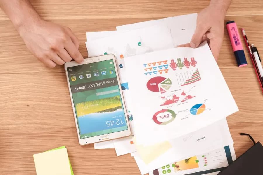 Printed charts on a desk beside a tablet