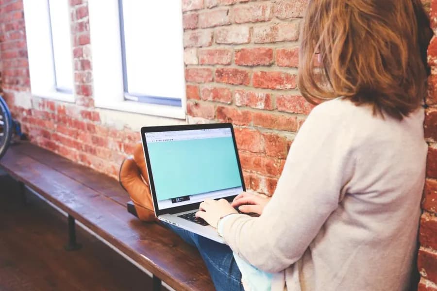 A person working at a laptop against a brick wall