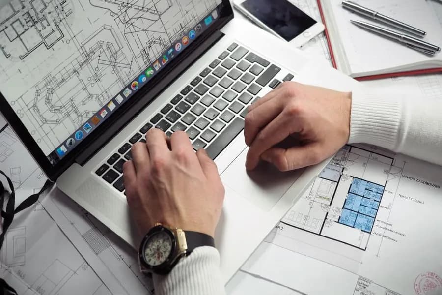 Technical plans spread on a desk beside a laptop