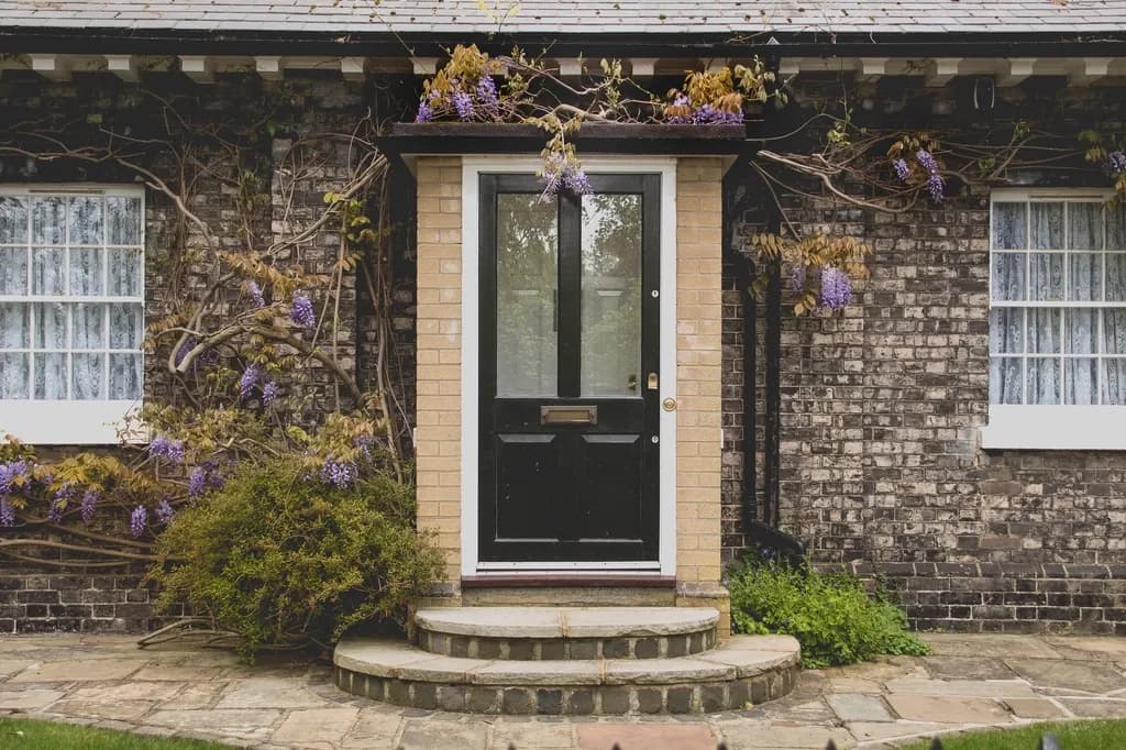 The front door of a brick house with a flowering shrub beside the step