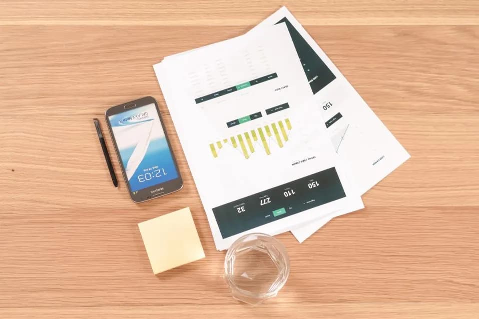 Printed financial reports on a desk beside a phone and notes