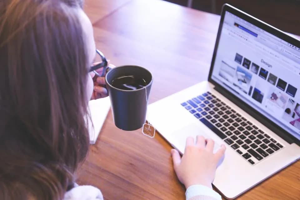A person working at a laptop with a coffee cup on the desk