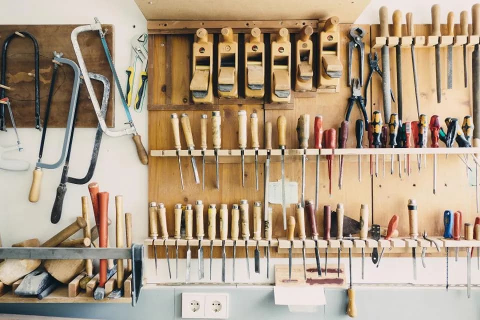 A workshop wall hung with hand tools above a bench