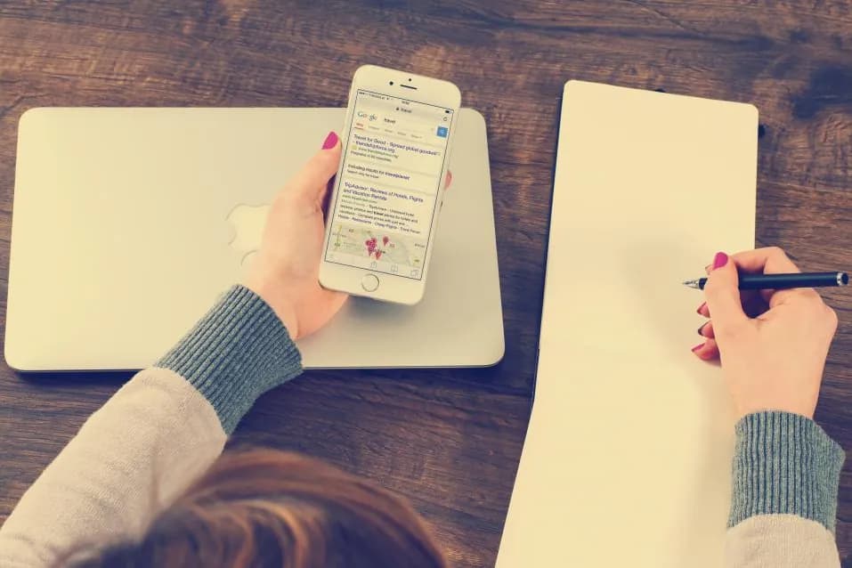 A person writing on a notepad with a phone resting beside it